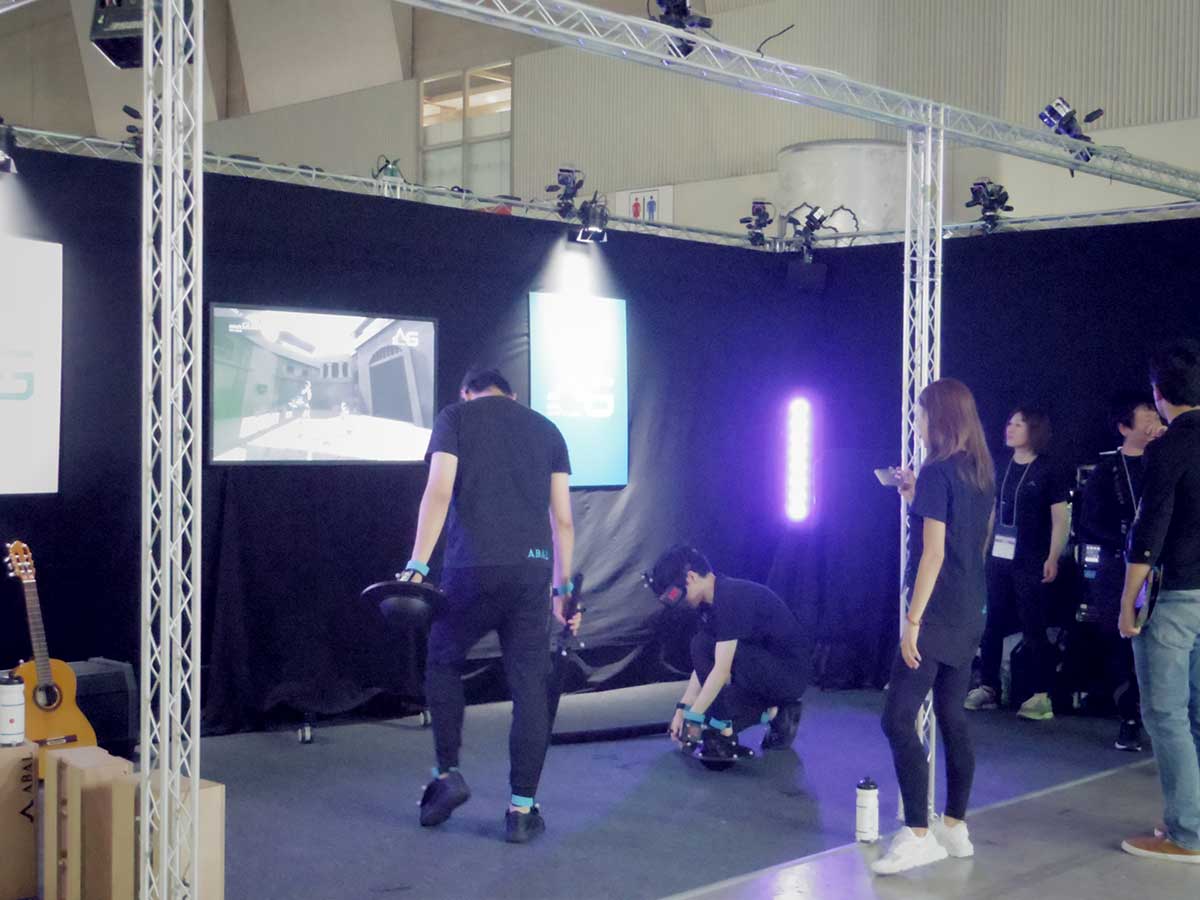 「東京ゲームショウ2018」（TGS2018）で、VR機器の老舗のひとつであるクレッセントのブースでモーションキャプチャデバイスを使ったデモが行われている写真。